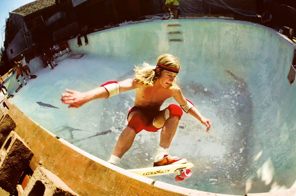 A skateboarder riding high along the edge of an empty swimming pool